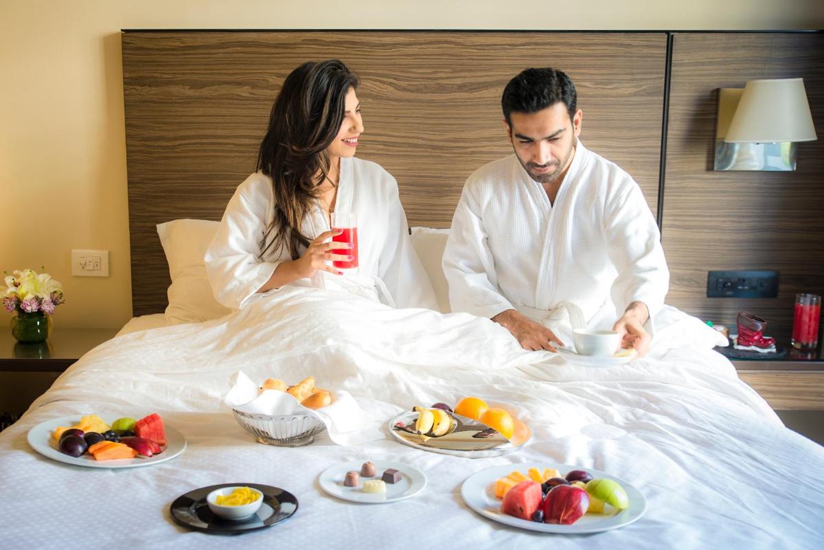 a man and woman sitting in bed with plates of food at Grand Hyatt Mumbai Hotel and Residences in Mumbai