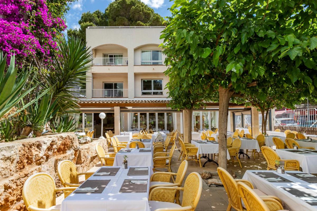 Un restaurante con mesas y sillas blancas y un edificio. en Houm Plaza Son Rigo, en Playa de Palma