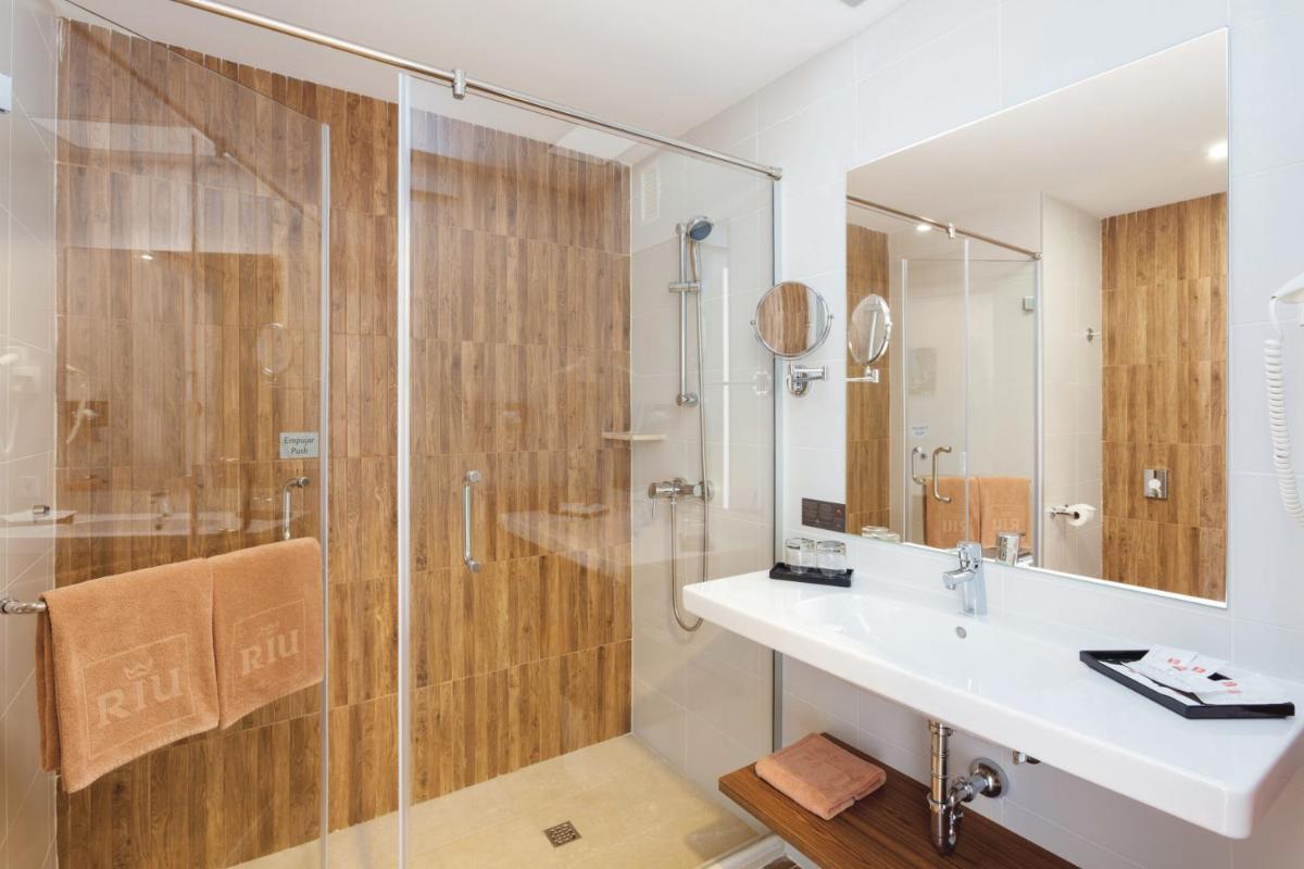 Un baño con ducha, lavabo y espejo. en Hotel Riu Arecas - Adults Only, en Adeje