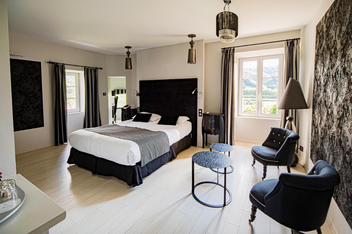 une chambre avec un grand lit et deux chaises dans l'établissement Château de la Falque, The Originals Relais, à Saint-Geniez-dʼOlt