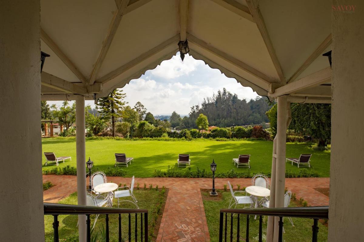 a porch with white tables and chairs and a green field at Savoy - IHCL SeleQtions in Ooty
