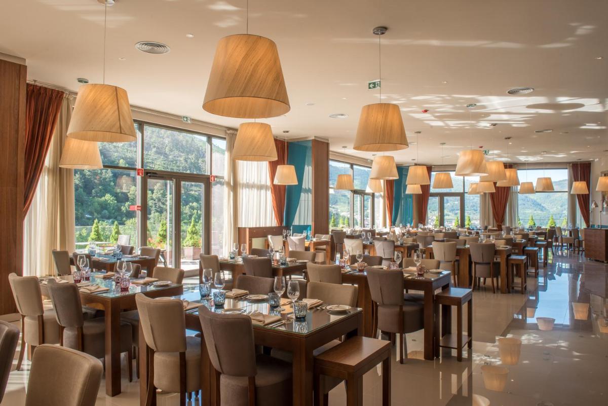 uma sala de jantar com mesas, cadeiras e janelas em Vila Galé Collection Serra da Estrela em Manteigas