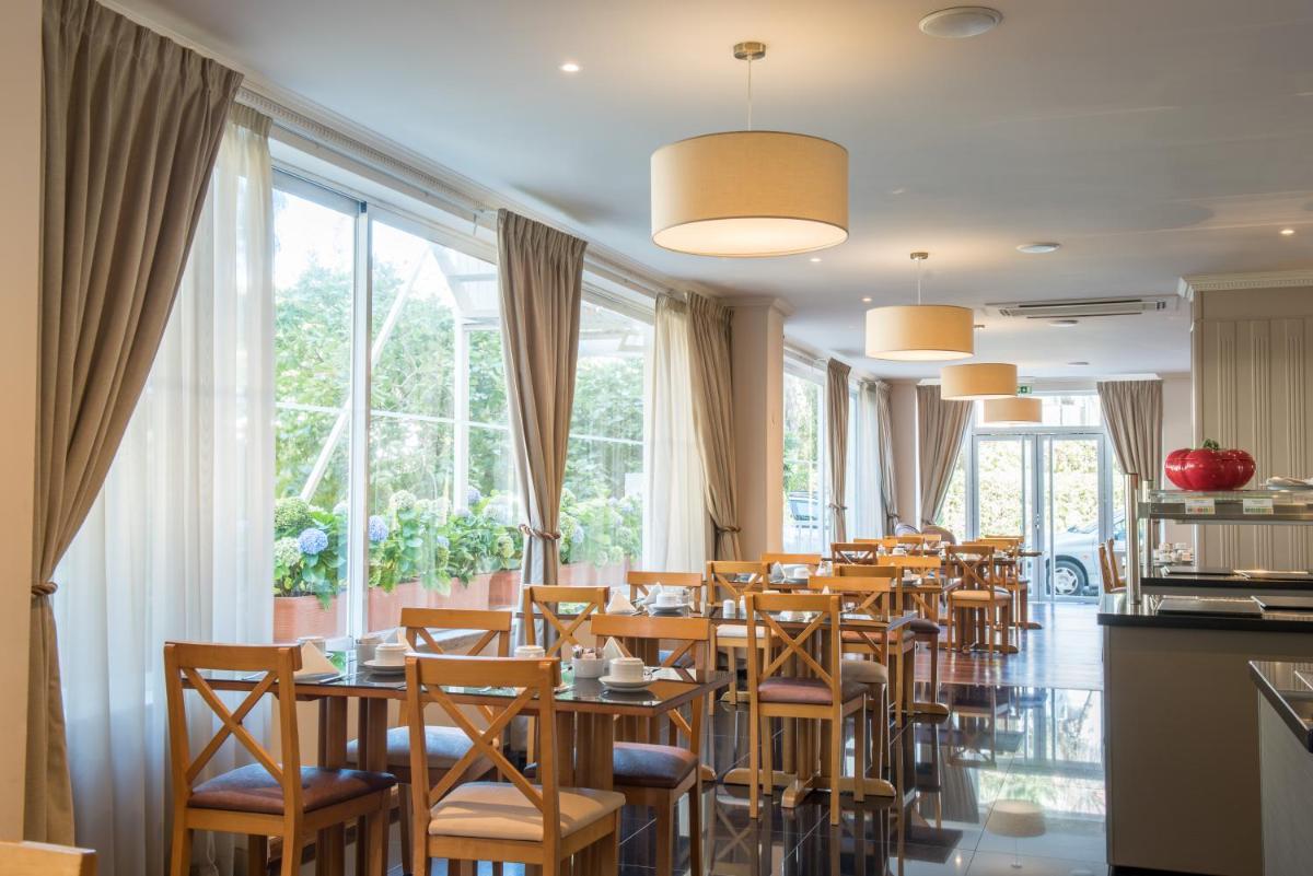 um restaurante com mesas e cadeiras de madeira e janelas em Vila Galé Estoril em Estoril