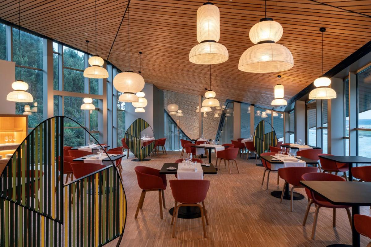 Un restaurante con mesas y sillas y grandes ventanales. en Parador Costa da Morte, en Muxía
