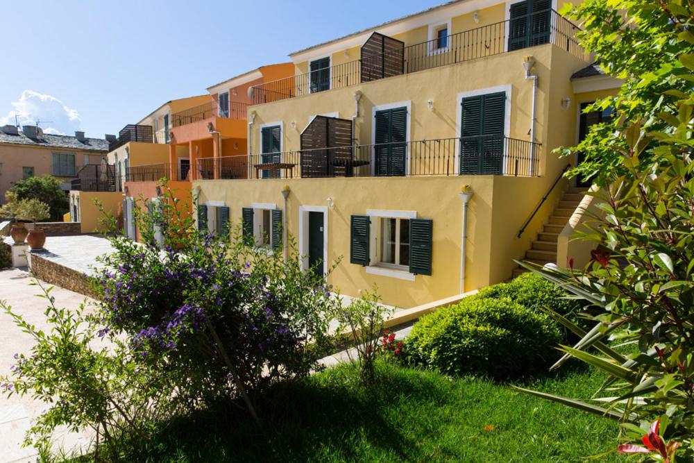 un bâtiment jaune avec un balcon et quelques buissons dans l'établissement Erbalunga - Résidence Les Bosquets - Cap corse Location, à Brando