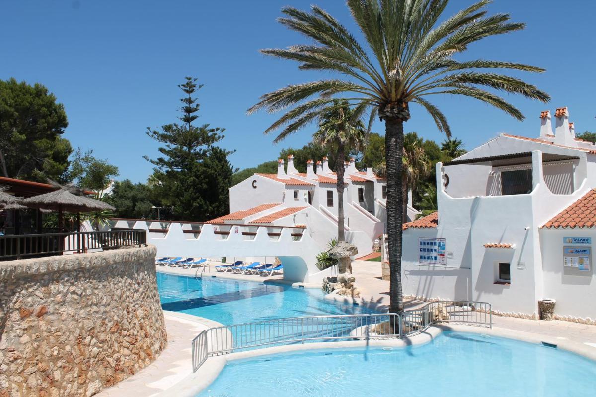 Una piscina con una palmera al lado de un edificio. en Apartaments Talayot, en Cala en Blanes