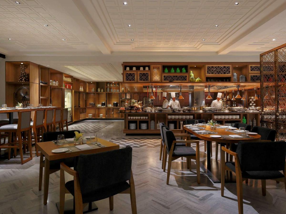 a restaurant with tables and chairs and a kitchen at Novotel Chennai Chamiers Road in Chennai