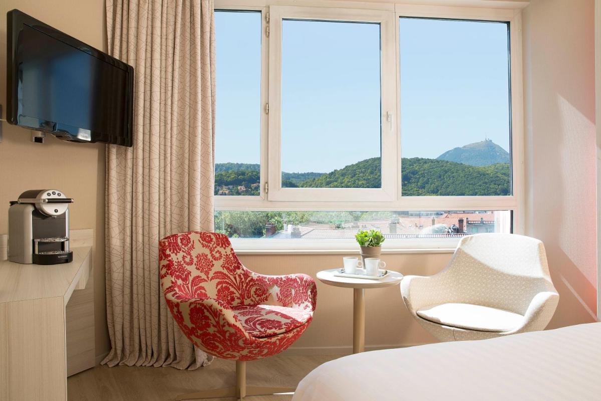 une chambre d'hôtel avec une chaise et une télévision dans l'établissement Oceania Clermont Ferrand, à Clermont-Ferrand
