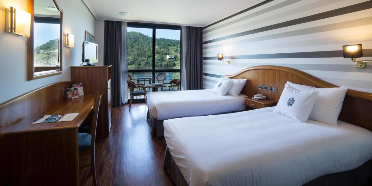 Una habitación de hotel con dos camas y un escritorio. en Laias Caldaria hotel y Balneario, en Laias