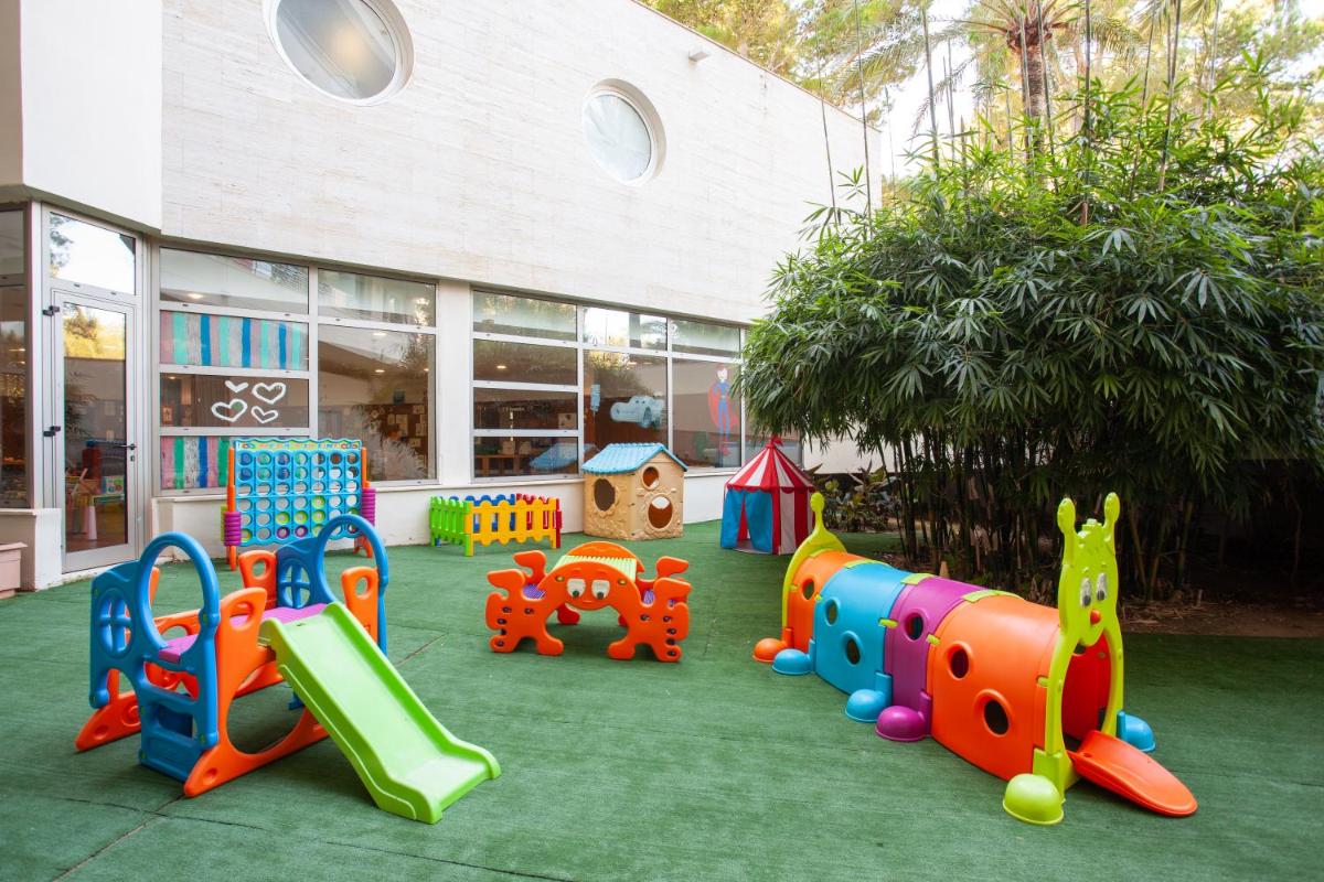 Un patio de juegos con diferentes tipos de equipos de juego frente a un edificio. en Grupotel Natura Playa, en Playa de Muro