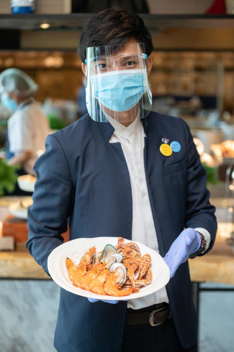 a person holding a plate of seafood with a mask on at Novotel Chennai Chamiers Road in Chennai