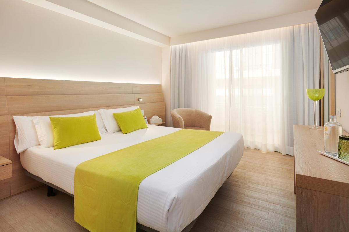 Una habitación de hotel con una cama grande con almohadas amarillas. en Hotel Sabina, en Cala Millor