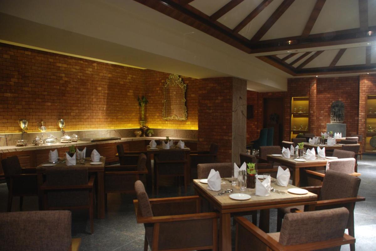 a restaurant with wooden tables and chairs and a brick wall at The Lalit Great Eastern Kolkata in Kolkata a restaurant with wooden tables and chairs and a brick wall at The Lalit Great Eastern Kolkata in Kolkata