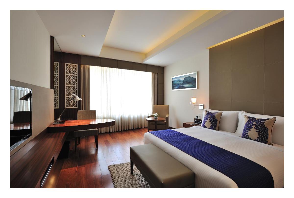 a hotel room with a large bed and a desk at The Anya Hotel-Golf Course Road in Gurgaon