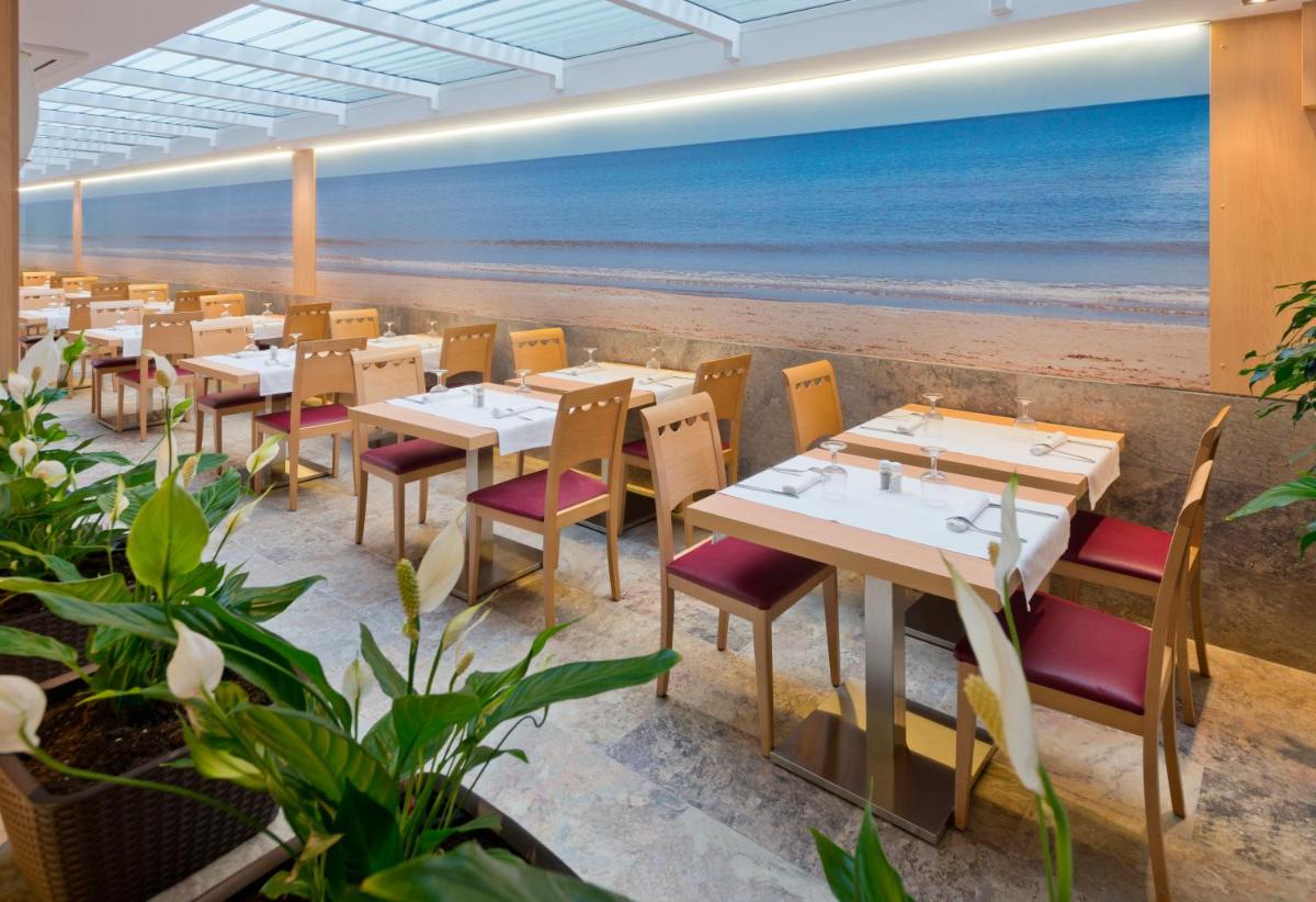 Un restaurante con mesas y sillas y la playa. en GHT Costa Brava & Spa, en Tossa de Mar