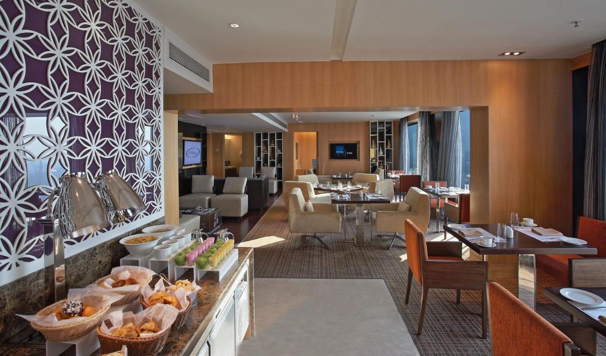a hotel lobby with a restaurant with tables and chairs at Novotel Pune Viman Nagar Road in Pune