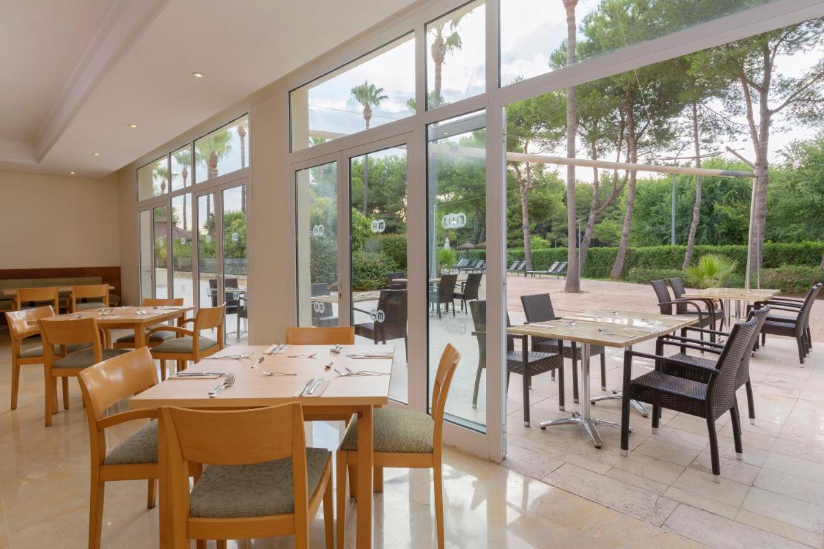 Un restaurante con mesas, sillas y ventanas. en HM Mar Blau, en Sa Coma