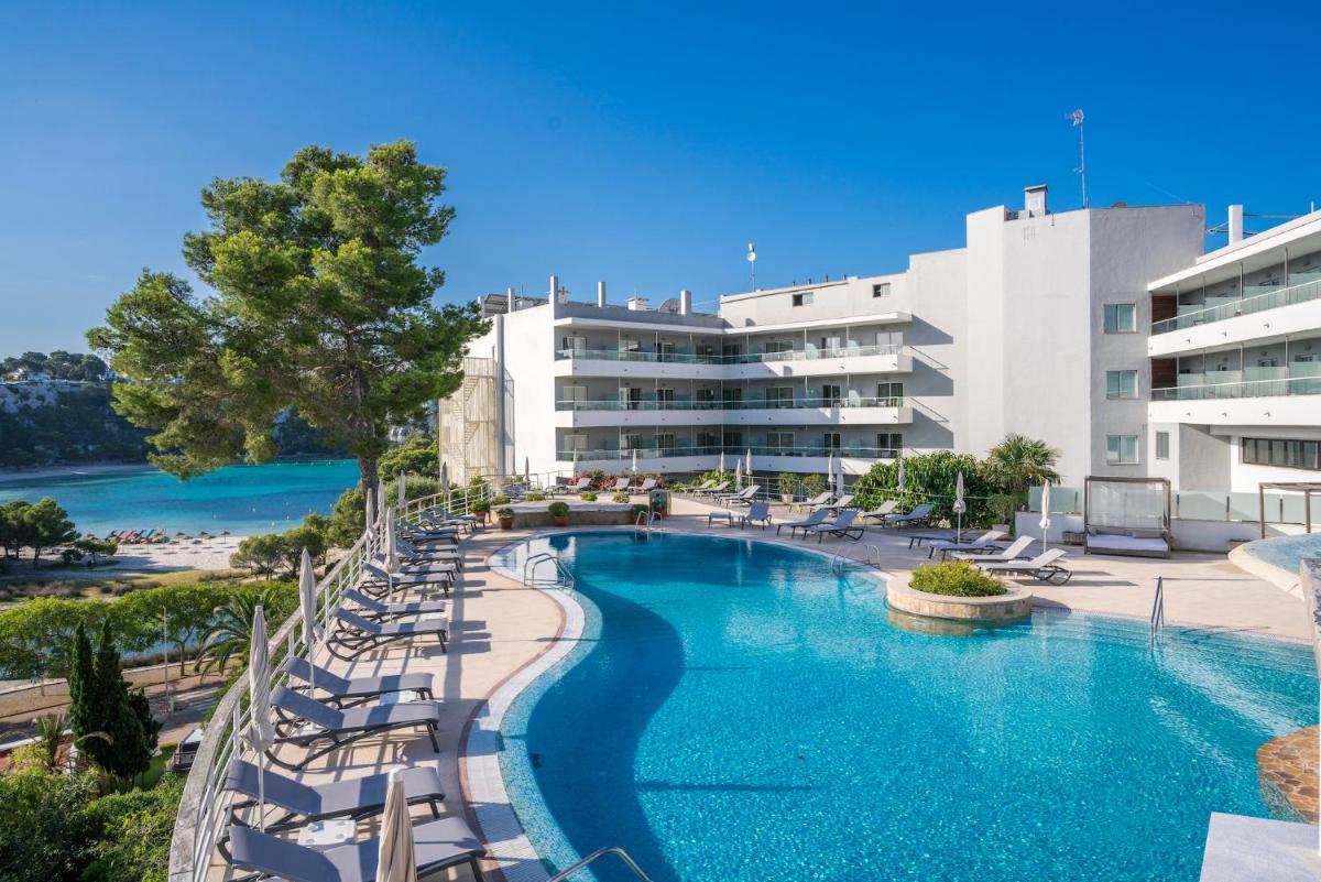 Una piscina con tumbonas frente a un edificio. en ARTIEM Audax - Adults Only, en Cala Galdana