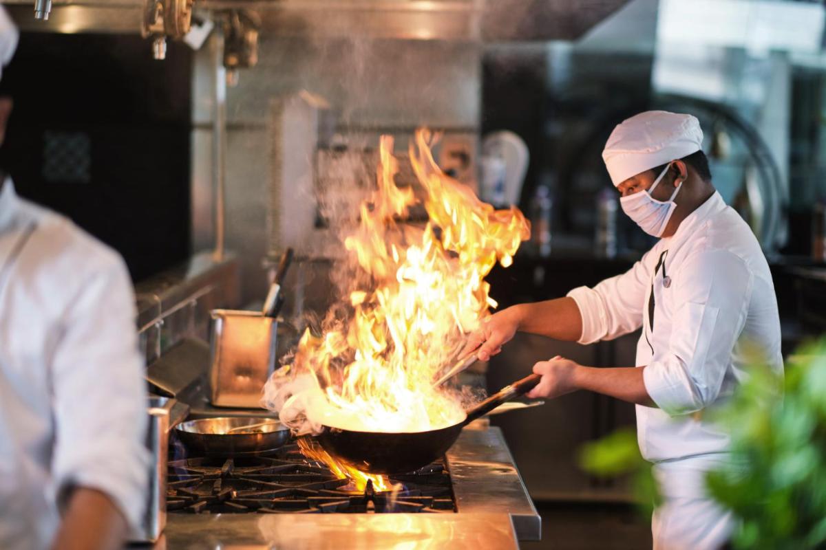 a chef cooking food in a pan on a grill at Hyatt Regency Kolkata in Kolkata a chef cooking food in a pan on a grill at Hyatt Regency Kolkata in Kolkata