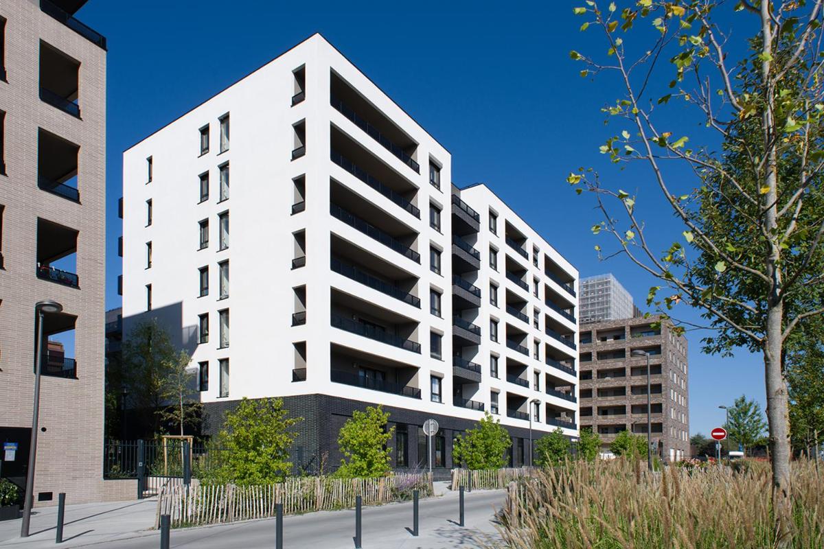 un immeuble d'appartements blanc devant quelques bâtiments dans l'établissement Domitys - Galilée, à Cergy