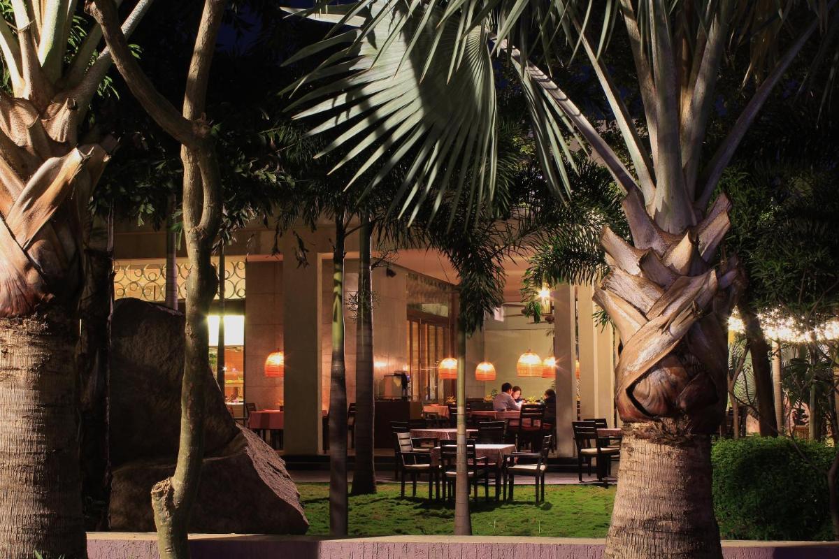 a restaurant with palm trees and a table and chairs at Hyatt Hyderabad Gachibowli in Hyderabad