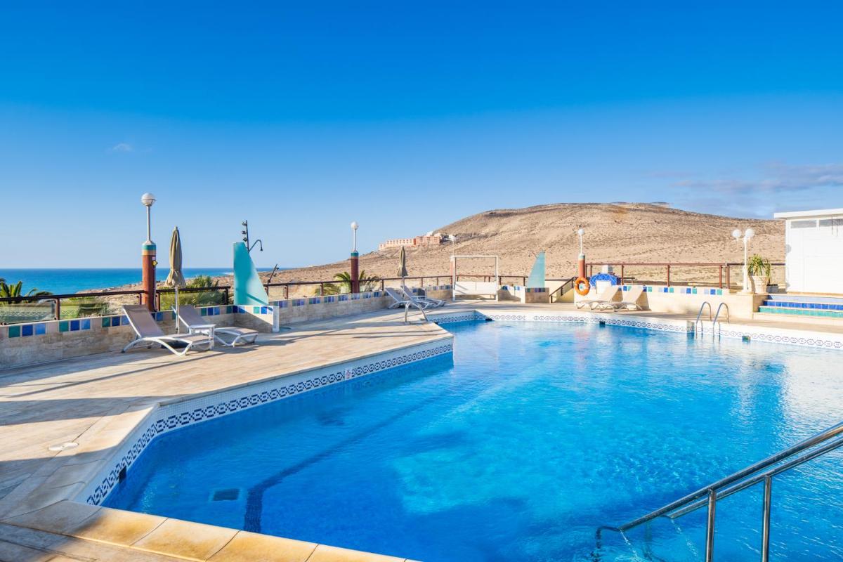 Una piscina con sillas y el océano al fondo. en Hotel Esmeralda Maris by LIVVO, en Costa Calma