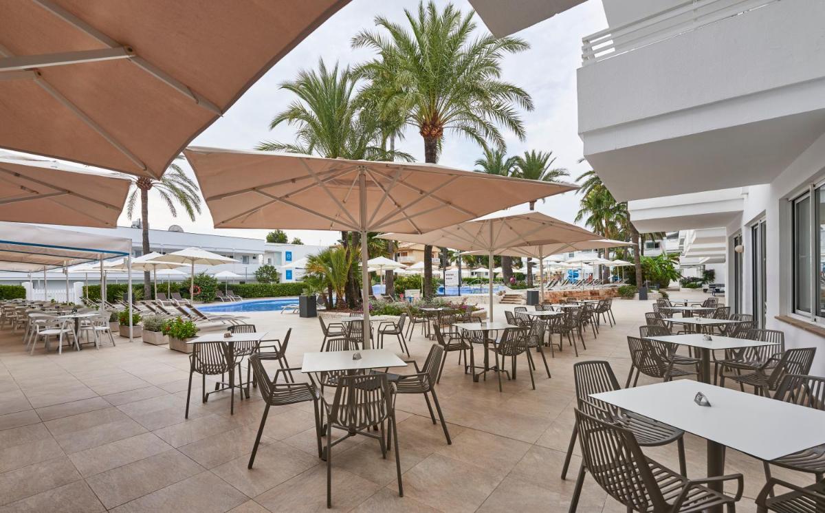 Un patio al aire libre con mesas, sillas y sombrillas. en Hoposa Hotel & Apartaments VillaConcha, en Puerto Pollensa