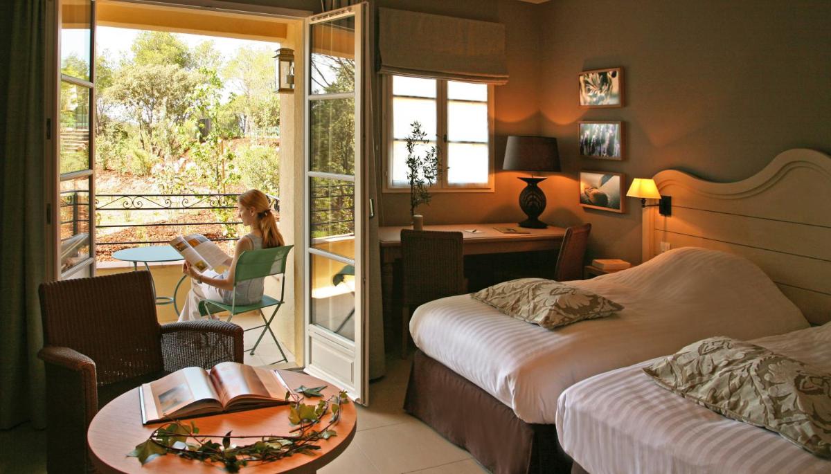 une chambre d'hôtel avec deux lits et une femme assise dans une chaise dans l'établissement Le Domaine de Saint Endreol Golf & Spa Resort, à La Motte