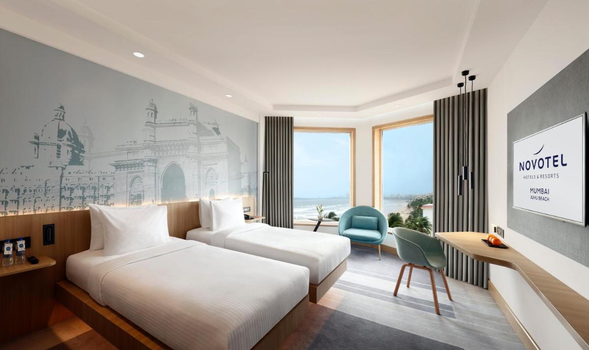 a hotel room with two beds and a desk at Novotel Mumbai Juhu Beach in Mumbai