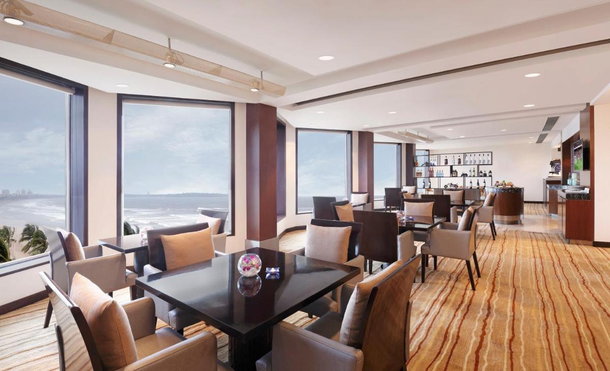 a dining room with tables and chairs and large windows at Novotel Mumbai Juhu Beach in Mumbai