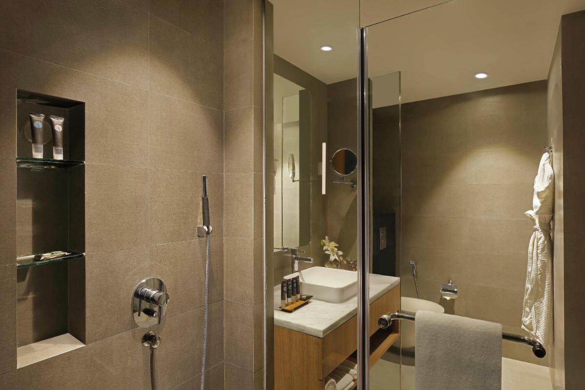 a bathroom with a shower with a sink and a mirror at Novotel Mumbai Juhu Beach in Mumbai