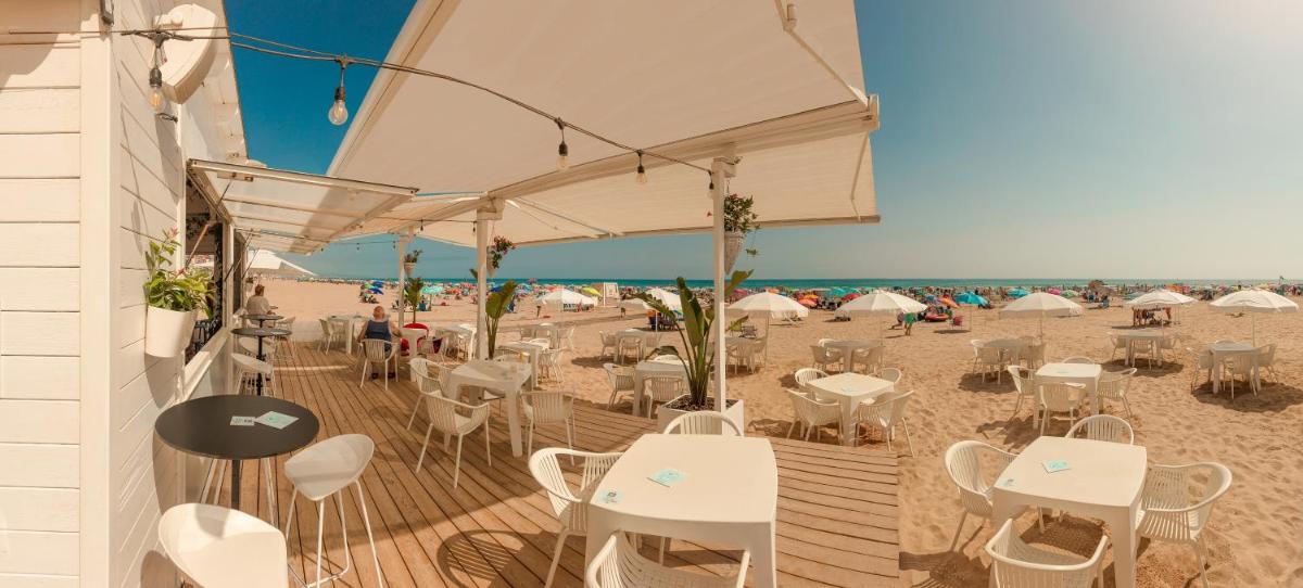un restaurante en la playa con mesas y sillas blancas en Hotel RH Gijón & Spa, en Gandía