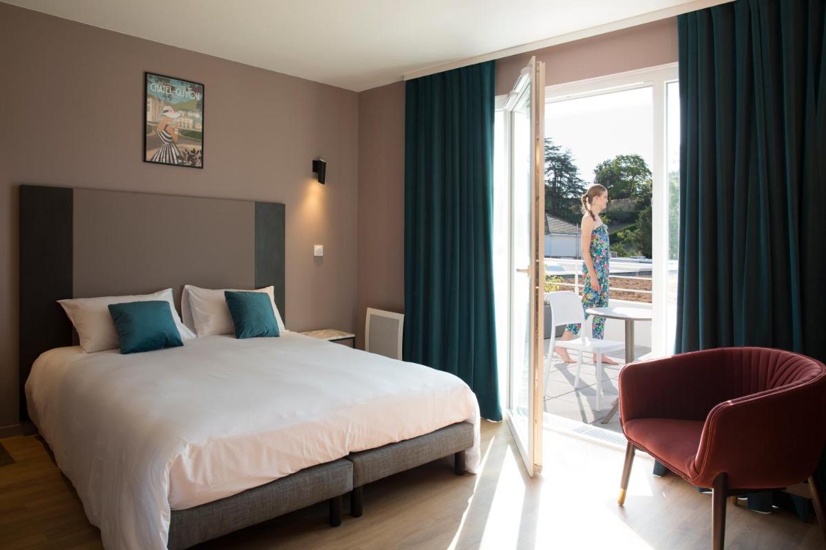 une chambre d'hôtel avec un lit et une femme qui regarde par la fenêtre dans l'établissement Résidence-Aïga Resort thermal & spa, à Châtel-Guyon