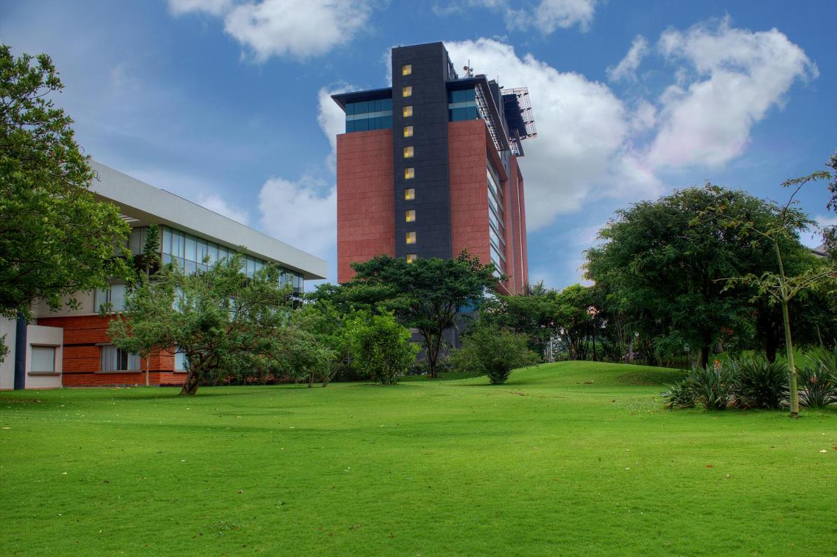 a tall building with a green field in front of a building at The Oterra in Bengaluru
