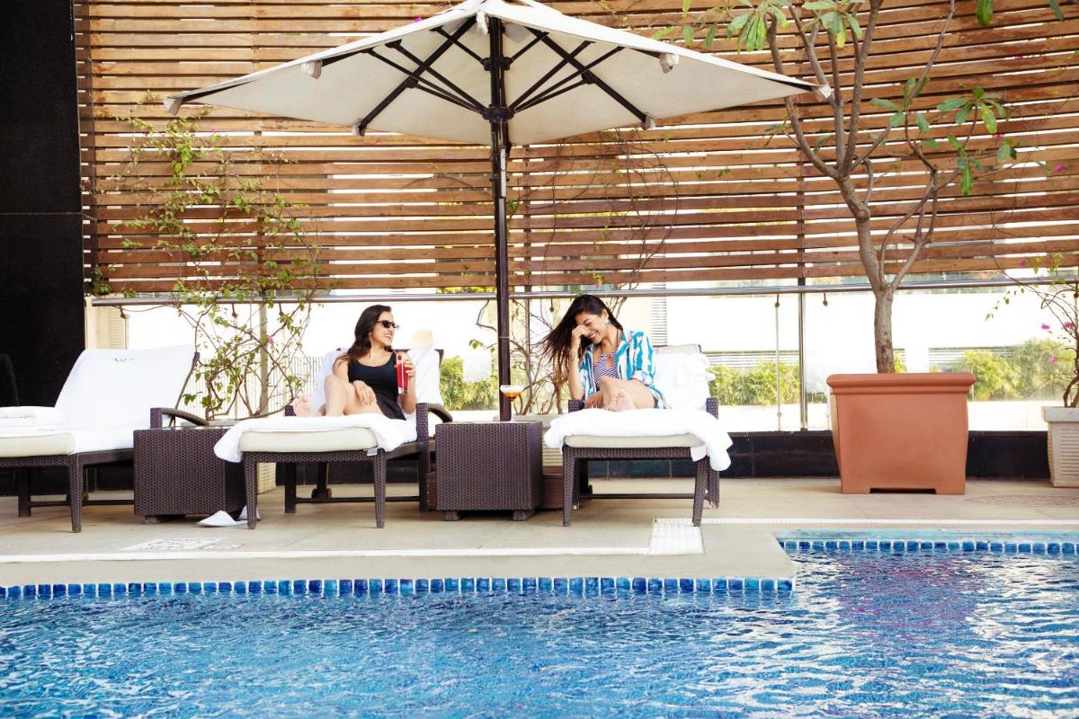 two women sitting in chairs next to a swimming pool at Sofitel Mumbai BKC in Mumbai