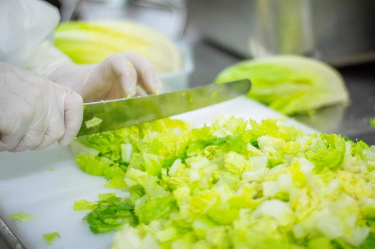 a person cutting lettuce with a knife on a cutting board at Sofitel Mumbai BKC in Mumbai