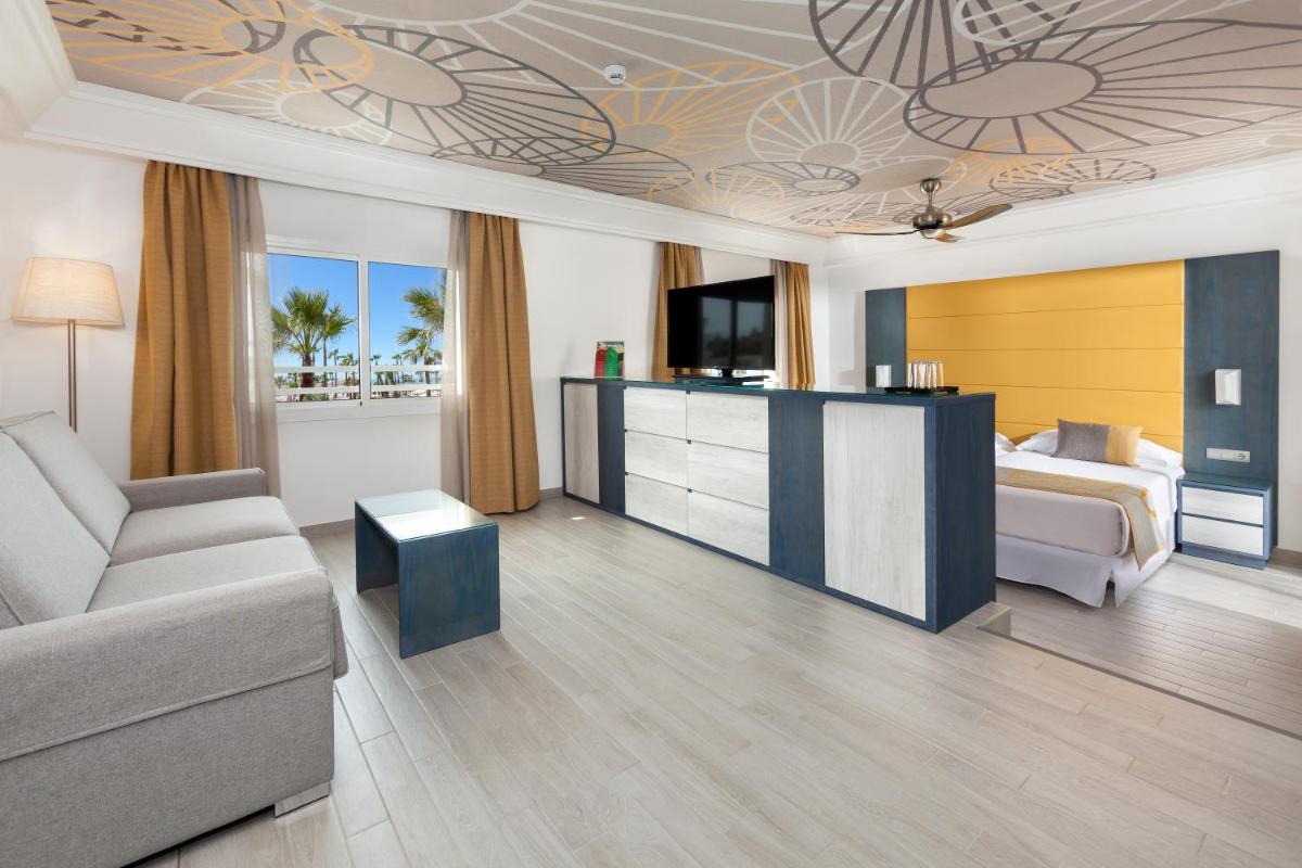 Una habitación de hotel con una cama, un sofá y un televisor. en Hotel Riu Chiclana - All Inclusive, en Chiclana de la Frontera