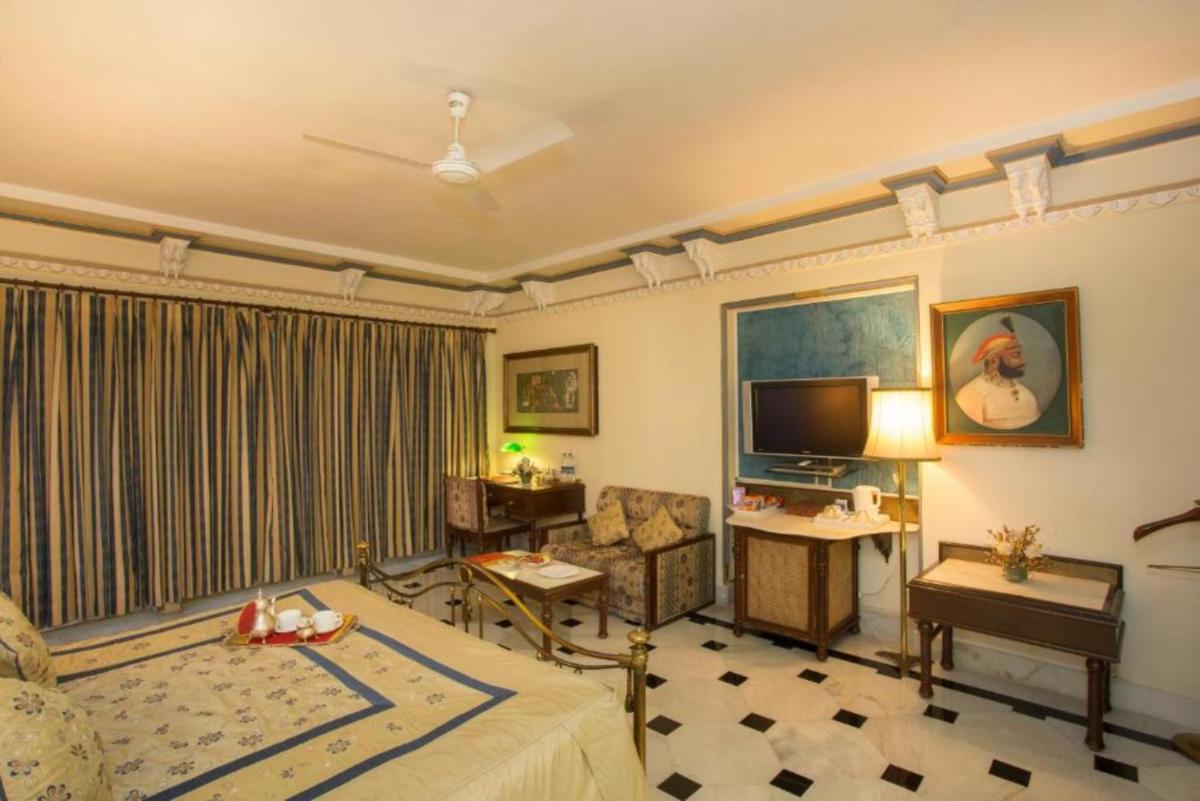 a hotel room with a bed and a television and a living room at Shiv Niwas Palace by HRH Group of Hotels in Udaipur