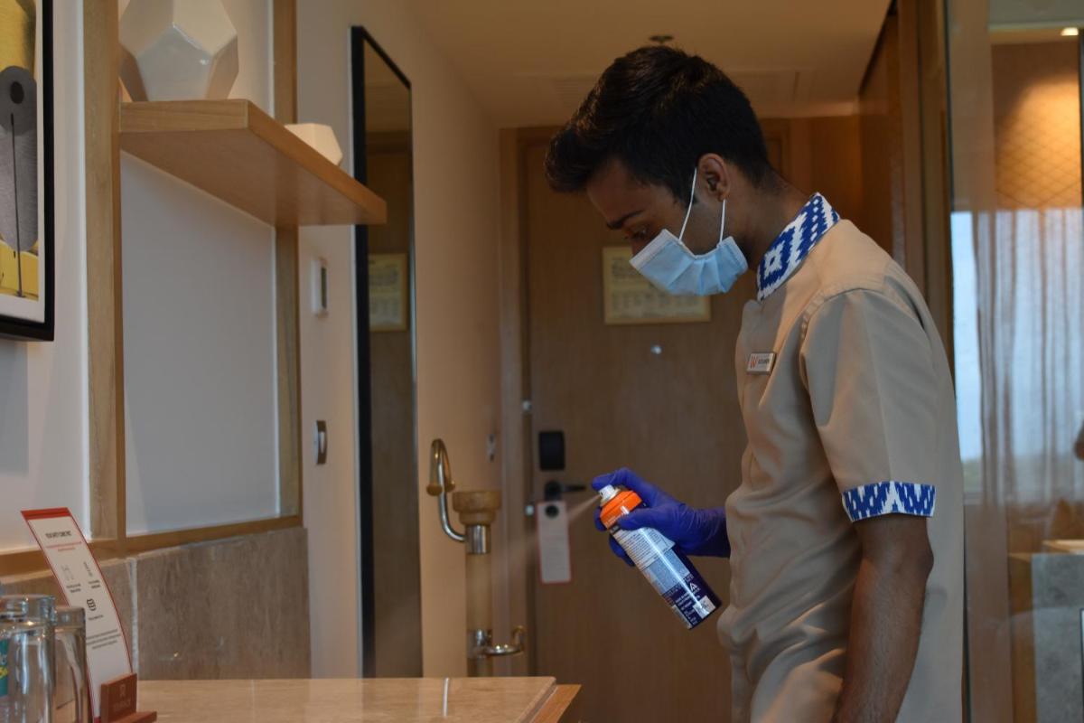 a man wearing a mask and gloves holding a bottle ofagent at Welcomhotel by ITC Hotels, RaceCourse, Coimbatore in Coimbatore