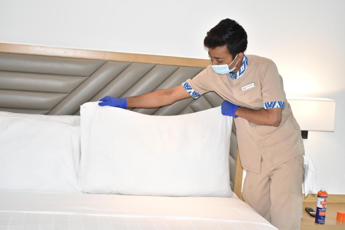 a man in a mask making a bed at Welcomhotel by ITC Hotels, RaceCourse, Coimbatore in Coimbatore