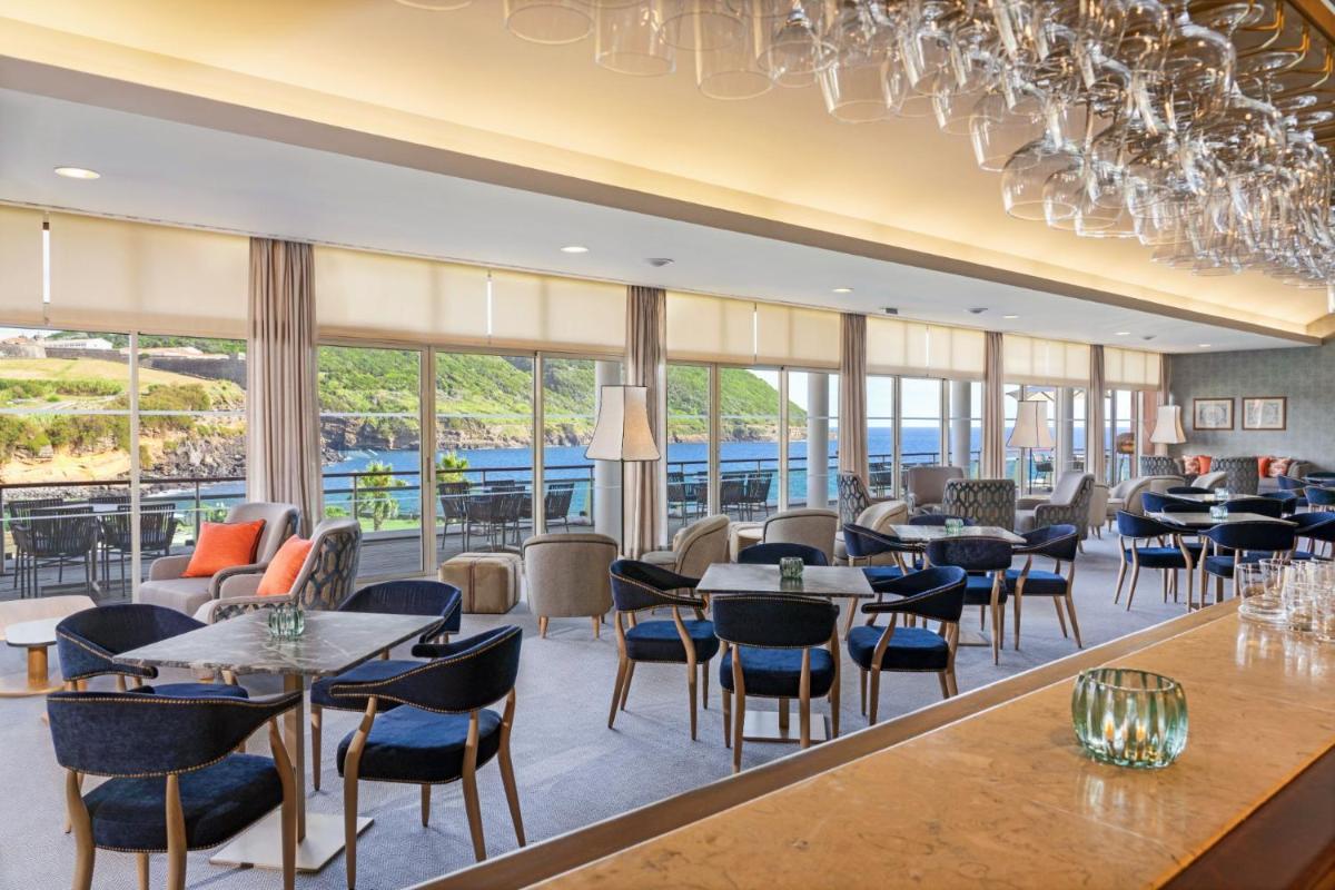 um restaurante com mesas, cadeiras e janelas em Terceira Mar Hotel em Angra do Heroísmo