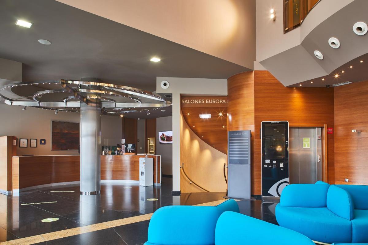 Un vestíbulo con sillas azules y un bar. en Silken Ciudad Gijón, en Gijón