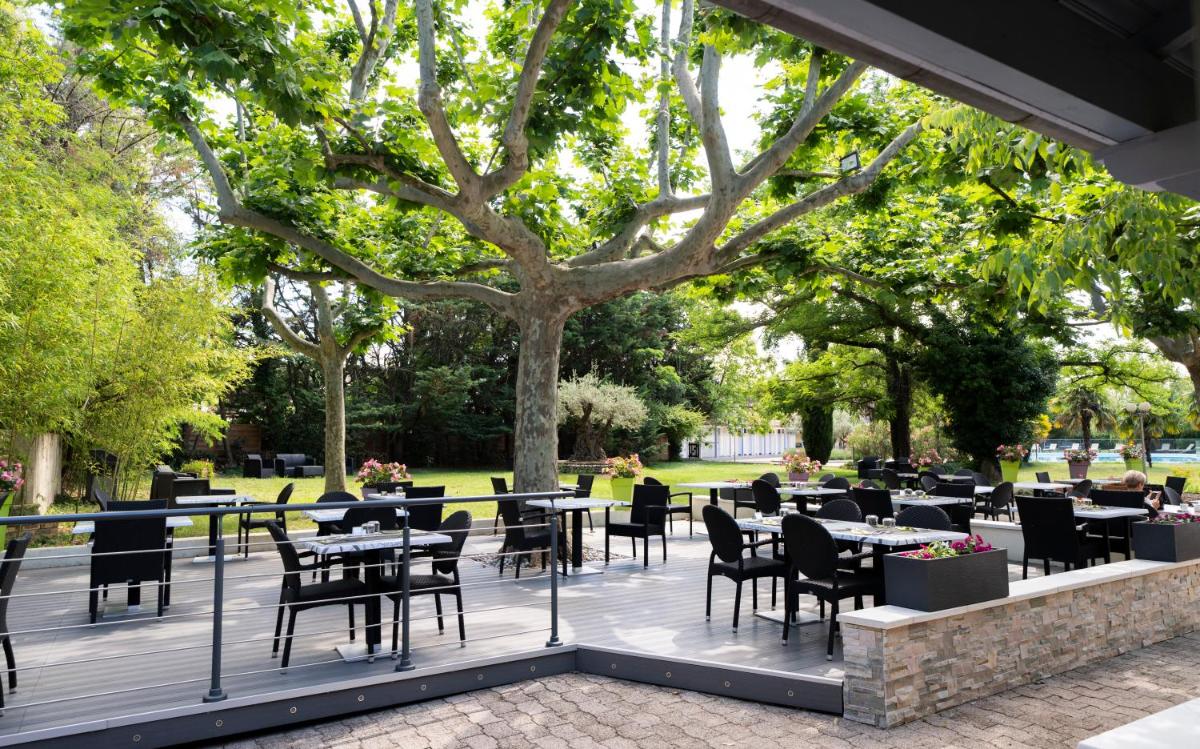 un patio avec tables et chaises dans un parc dans l'établissement Logis Hotel Restaurant SPA Les Oliviers, à Loriol-sur-Drôme
