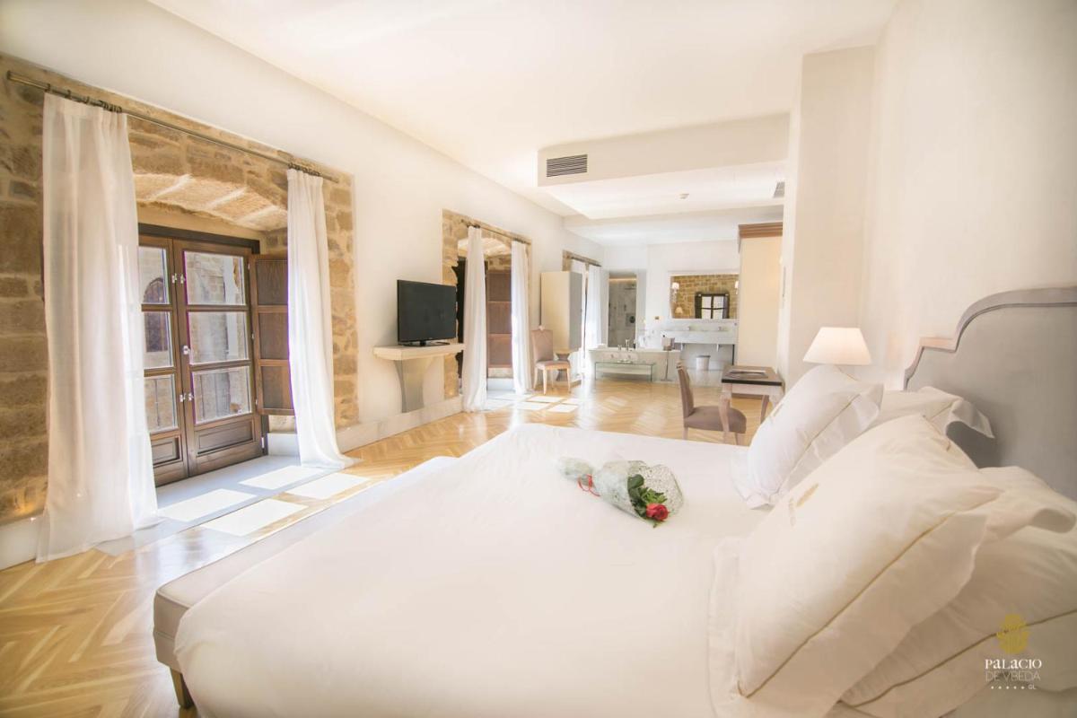 Un dormitorio con una cama blanca y una sala de estar. en Hotel Palacio De Úbeda 5 G.L, en Úbeda