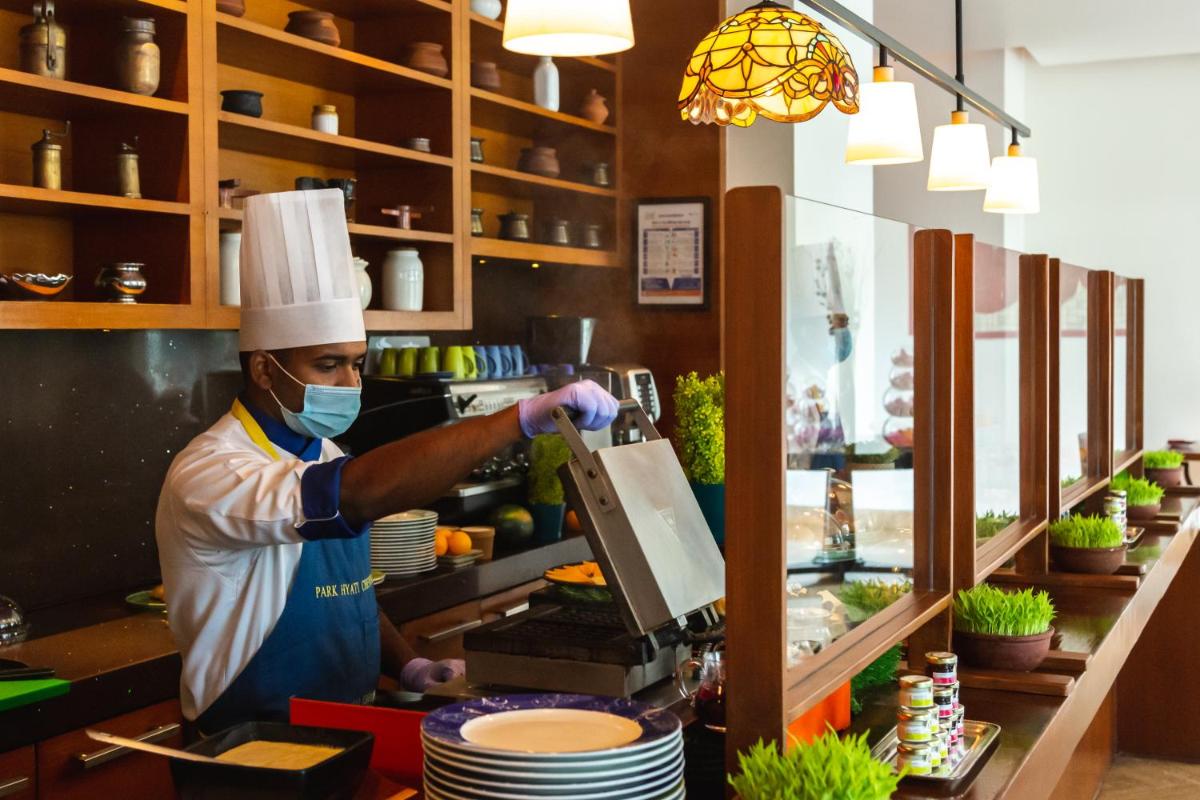a chef wearing a mask making food in a kitchen at Park Hyatt Chennai in Chennai