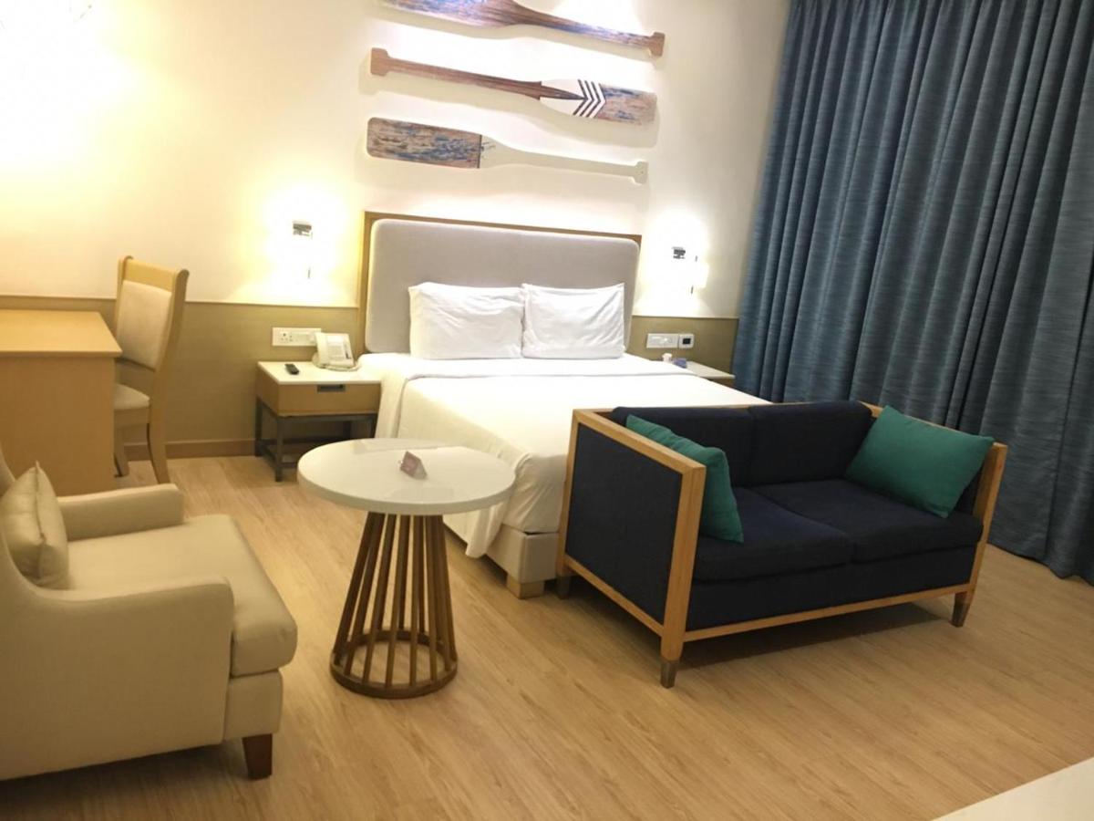 a bedroom with a bed and a couch and a chair at Radisson Goa Candolim in Candolim