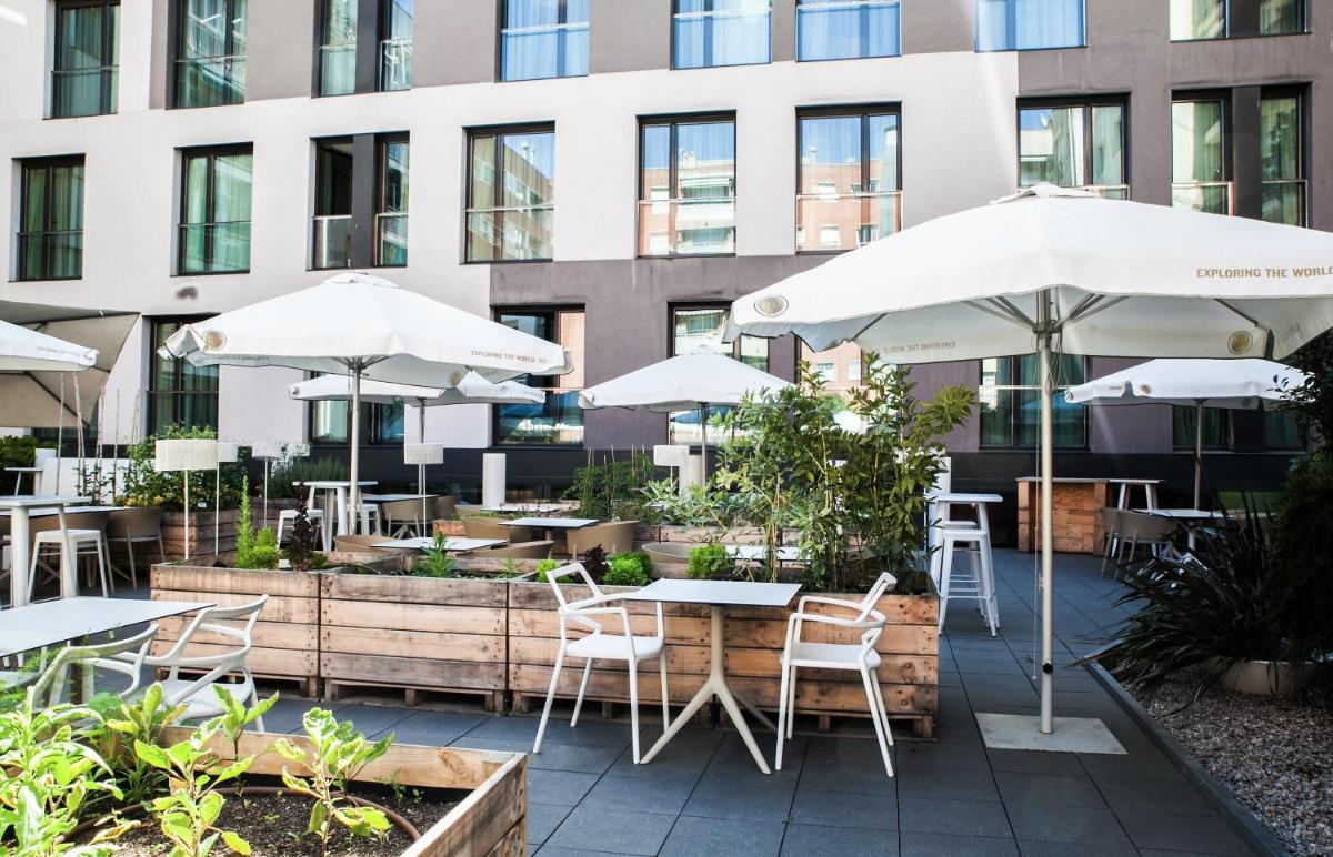 Un patio con mesas y sombrillas frente a un edificio. en Grums Hotel & Spa, en Barcelona