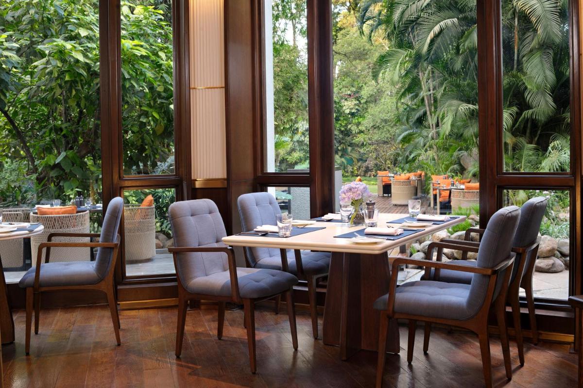 a dining room with a table and chairs and large windows at The Oberoi Bengaluru in Bengaluru a dining room with a table and chairs and large windows at The Oberoi Bengaluru in Bengaluru