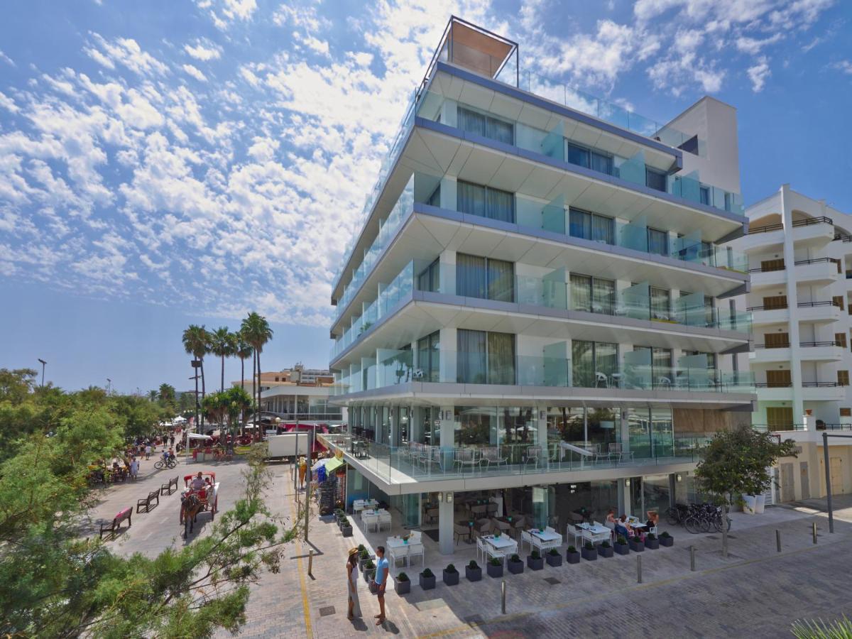 un edificio alto con gente sentada fuera de él en Kyrat Amarac - Adults Only, en Cala Millor