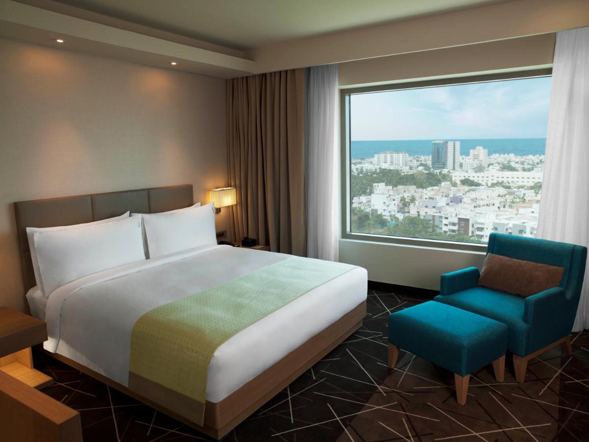 a hotel room with a bed and a chair and a large window at Holiday Inn Chennai OMR IT Expressway by IHG in Chennai